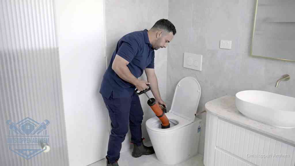 Een monteur buigt over een wandcloset en duwt met de hand een persluchtontstopper in de toiletpot om de verstopping handmatig los te maken in Arnhem