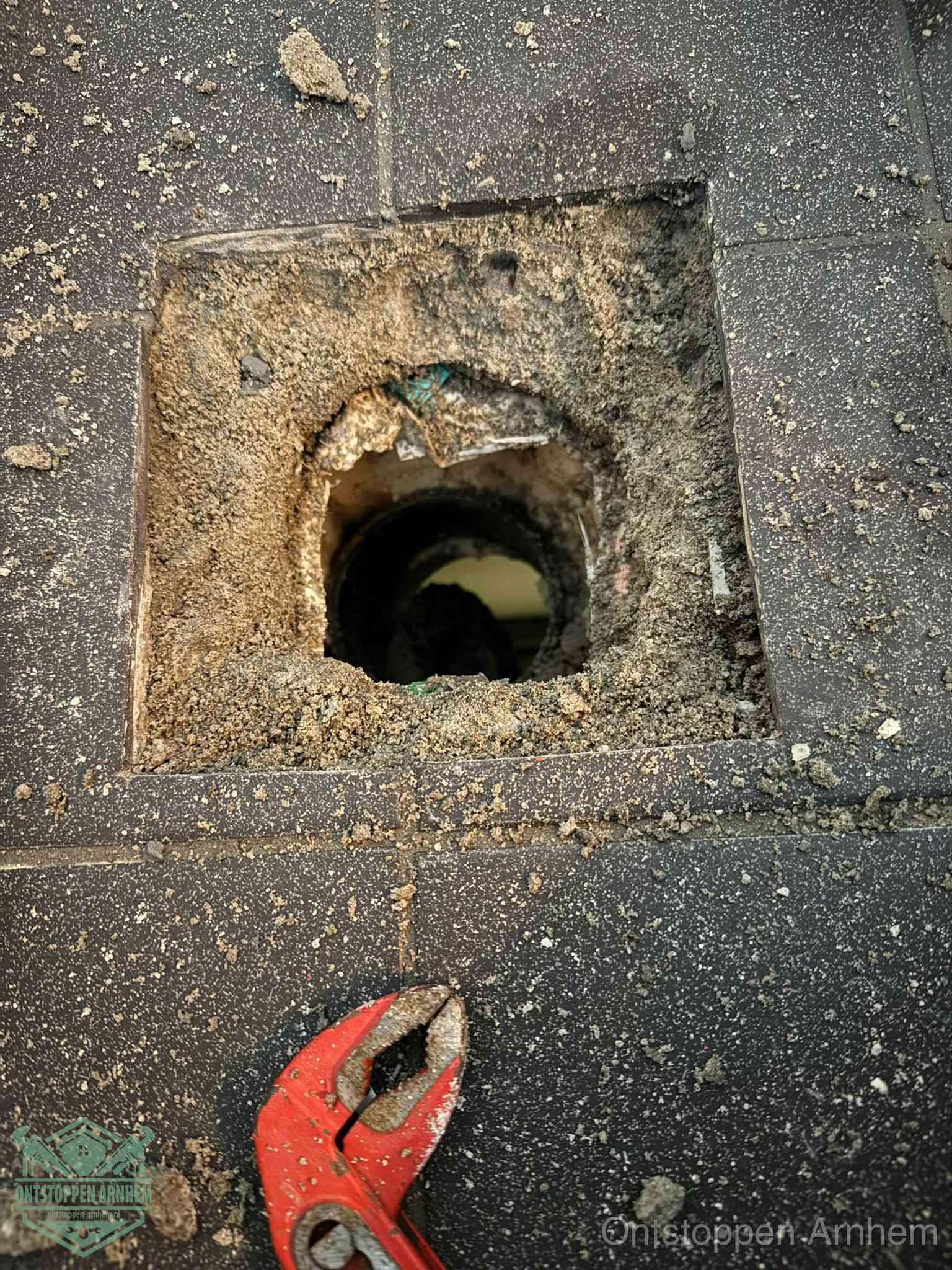 Een geopend rioolputje in een betontegelvloer met losgemaakt rooster en een zichtbare ronde afvoerbuis, het achterhalen waar de afvoerverstopping zit in Arnhem
