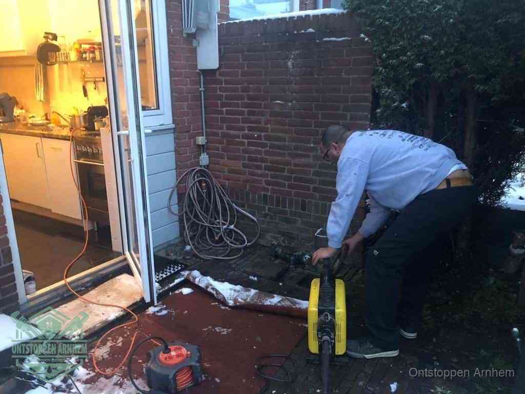 Een monteur werkt buiten bij een open riool-/grondput met een elektrische ontstoppingsmachine om een verborgen afvoerprobleem op te sporen in Arnhem