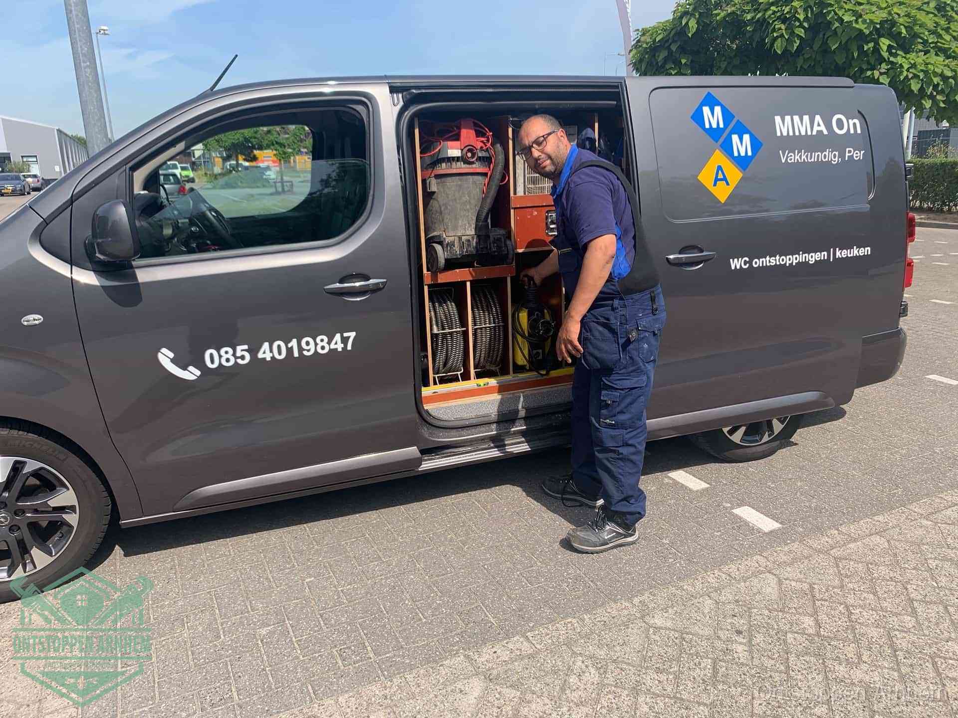 Een monteur bij de open schuifdeur van zijn bedrijfsbus op een parkeerplaats, klaar om de oorzaak van terugkerende afvoerverstoppingen aan te pakken in Arnhem