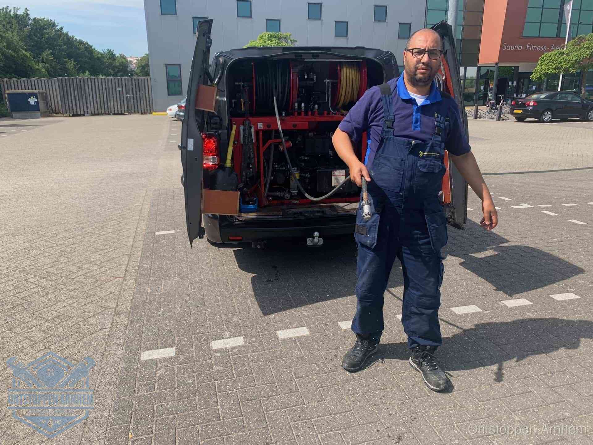Een monteur bij zijn bestelbus met een hogedruk- en rioolreinigingsunit, klaar om de oorzaak van terugkerende wc-verstoppingen aan te pakken in Arnhem