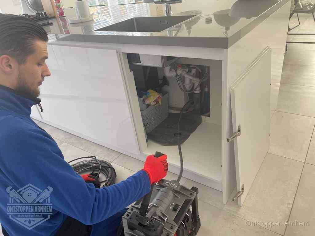 Monteur ontstopt met een veermachine een verstopte afvoer onder de gootsteen in Arnhem