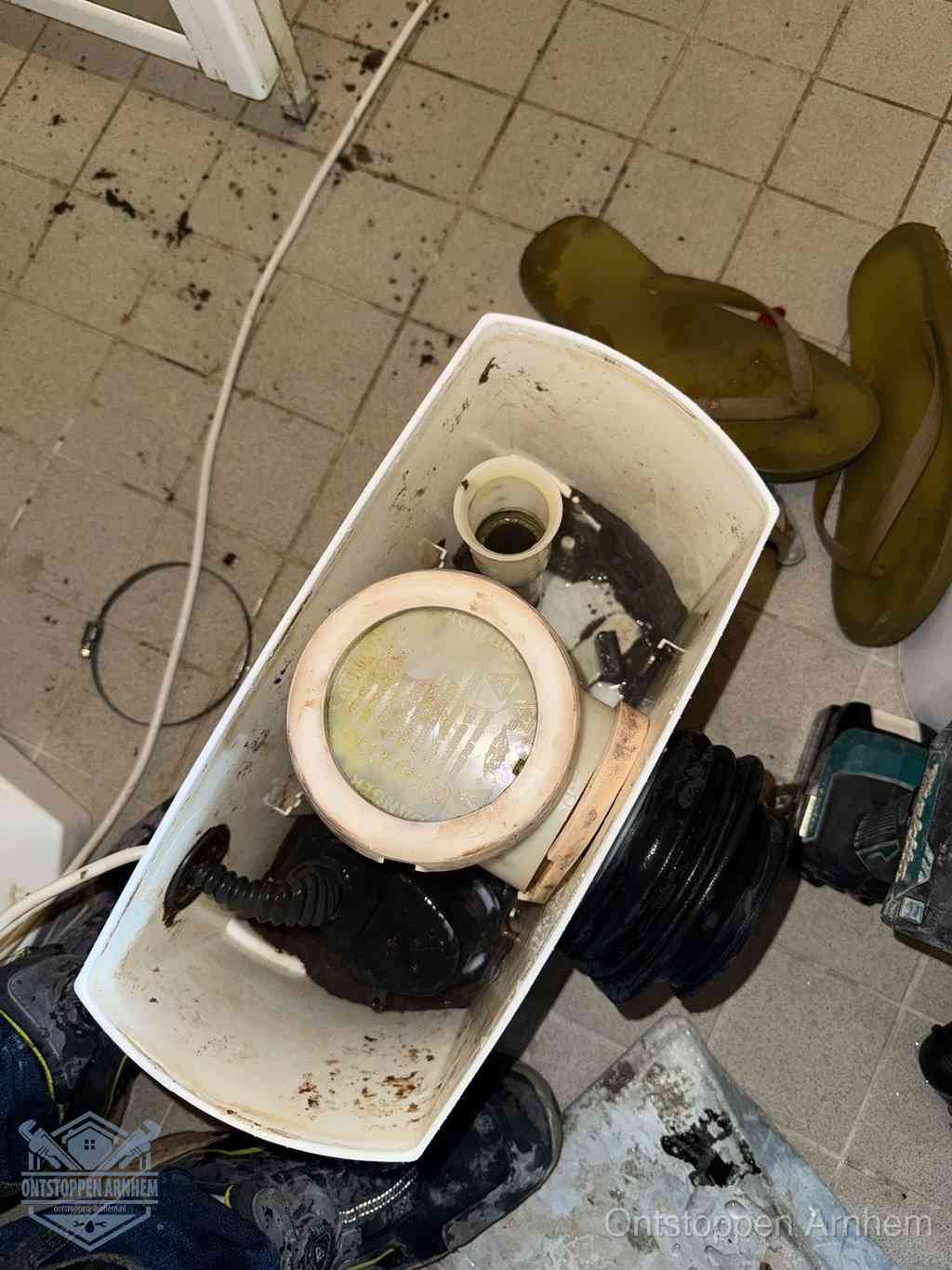 Een gedemonteerde toiletpot op de vloer met ontstoppingsveer en gereedschap ernaast, het verwijderen van een vastzittend voorwerp uit de wc in Arnhem