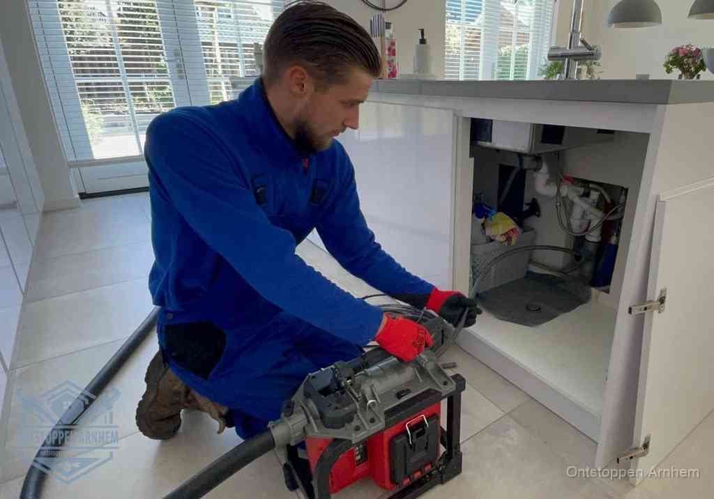 Een monteur voert een professionele elektrische ontstoppingsmachine in de afvoer onder de spoelbak tijdens het gootsteen ontstoppen in Arnhem