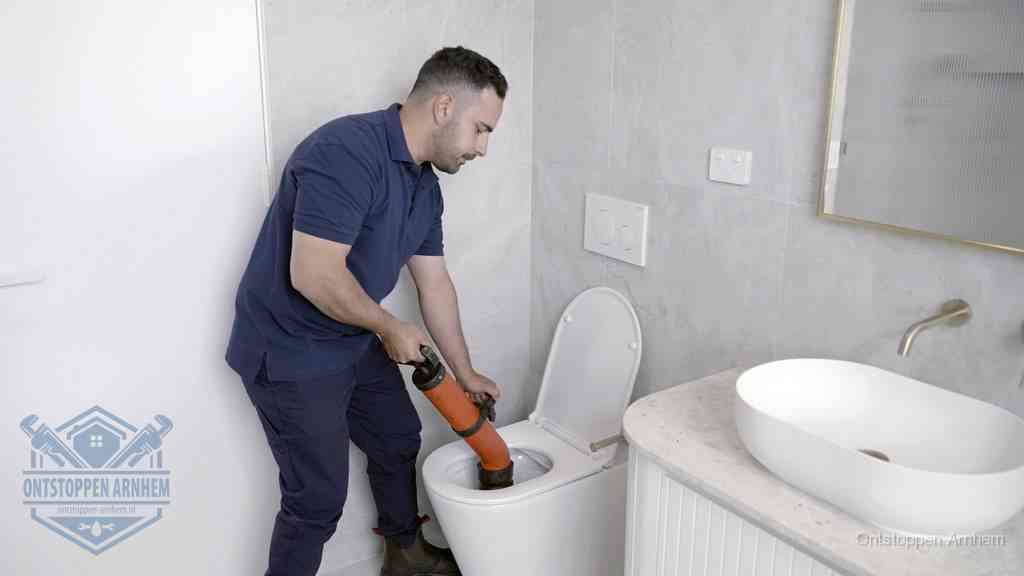 Een man gebruikt een handmatige luchtdruk-ontstopper in een modern betegeld toilet om zelf de wc te ontstoppen in Arnhem